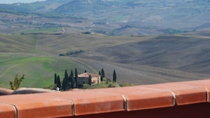 A breakfast table with orange juice, pastries, and a view of rolling hills in the background. - Casanova - Panoramic Rooms and Suites (San Quirico d'Orcia)