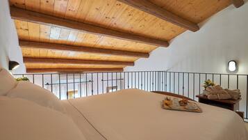 Een slaapkamer met een houten plafond, een bed met wit beddengoed, een dienblad met ontbijtartikelen en een balkon met een hekwerk.