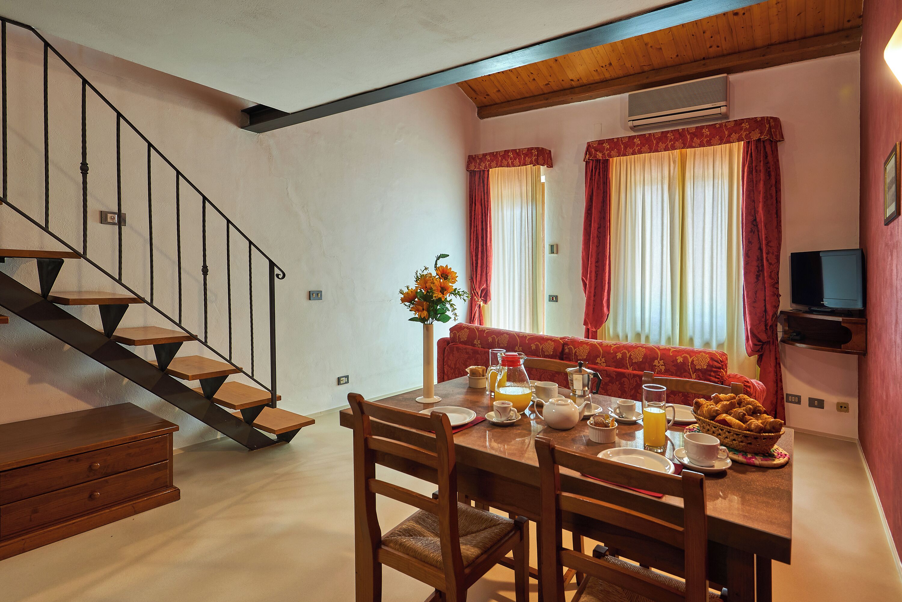 Un coin repas avec une table en bois mise pour le petit-déjeuner, un escalier et un canapé à l’arrière-plan.