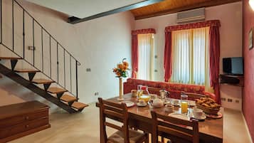Zona pranzo con tavolo in legno apparecchiato per la colazione, una scala e un divano sullo sfondo.