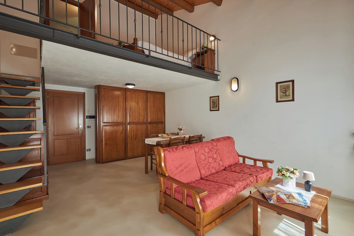 A spacious living area with a wooden sofa, a dining table, and a staircase leading to an upper level.