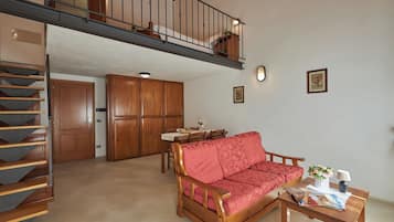 A spacious living area with a wooden sofa, a dining table, and a staircase leading to an upper level.