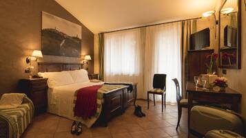 Habitación de hotel con cama, una silla, un escritorio con espejo, televisor y maleta.