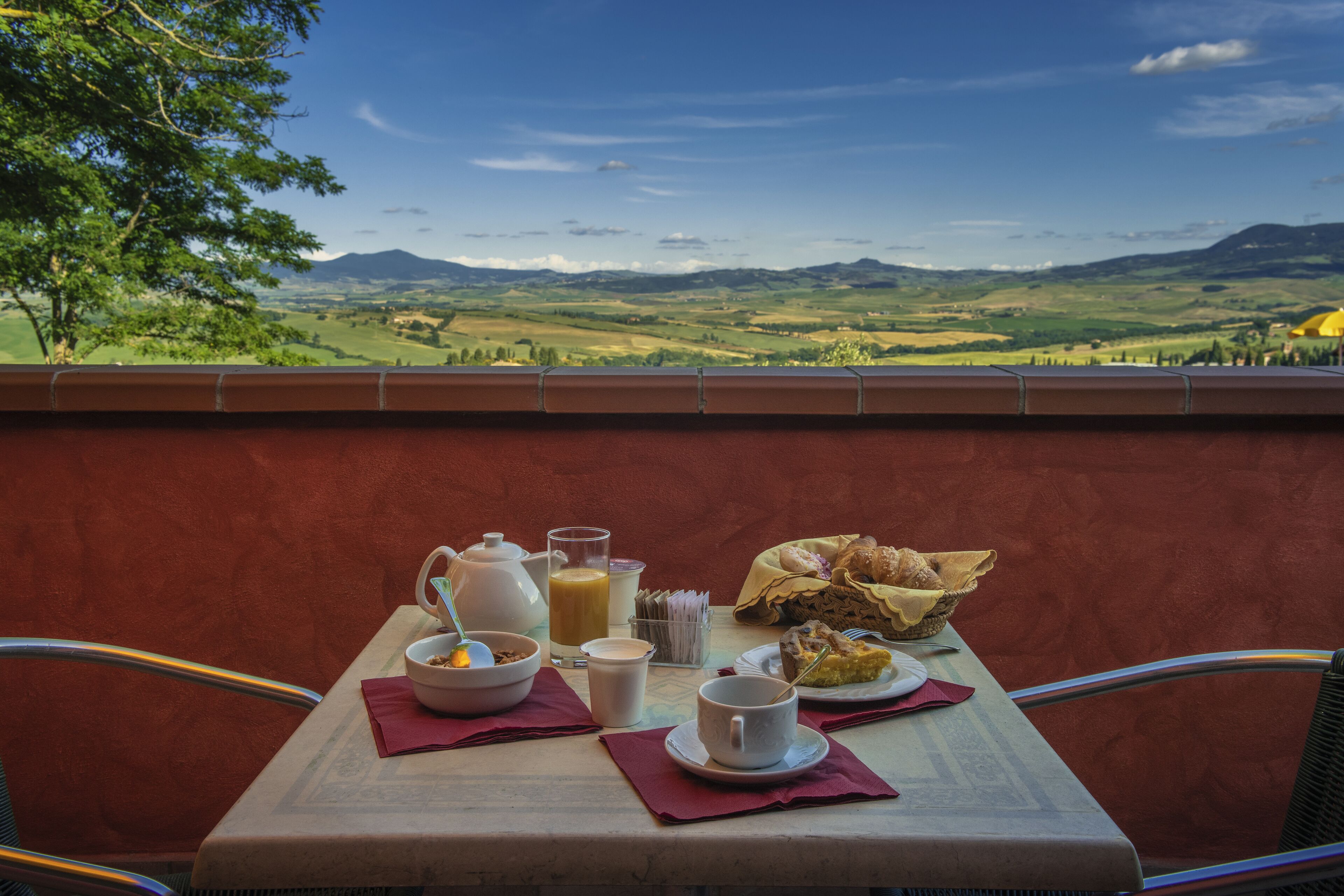 A table set with breakfast items, including a bowl of cereal, a cup of coffee, and a plate of food, overlooking a scenic landscape.