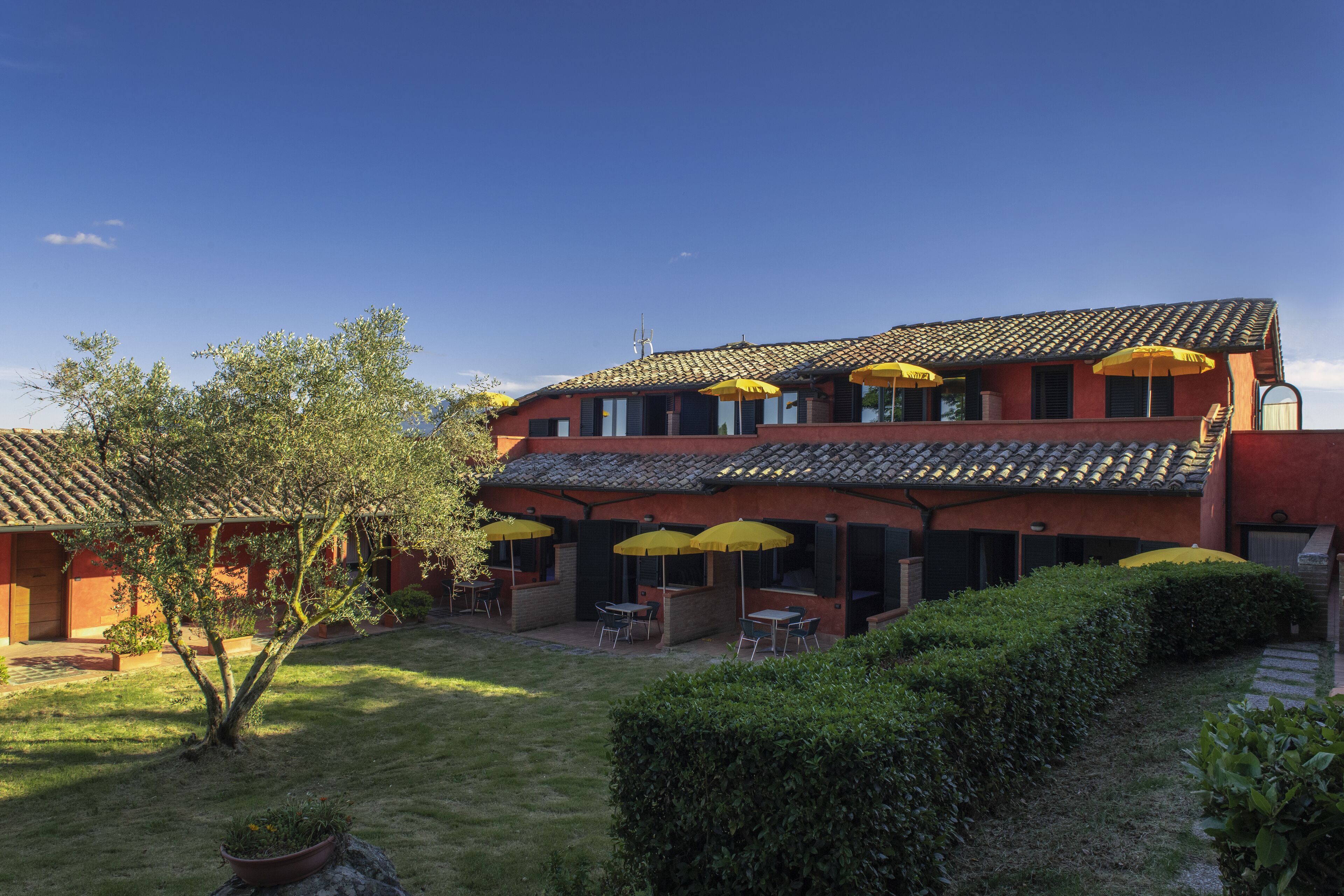Un edificio de dos pisos con fachada roja, varias ventanas y terraza al aire libre con sombrillas amarillas.
