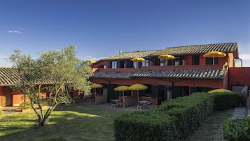 Un edificio de dos pisos con fachada roja, varias ventanas y terraza al aire libre con sombrillas amarillas.