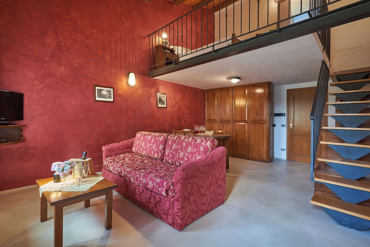 A living room with a red wall, a pink sofa, a wooden table with a vase and glasses, and a staircase.
