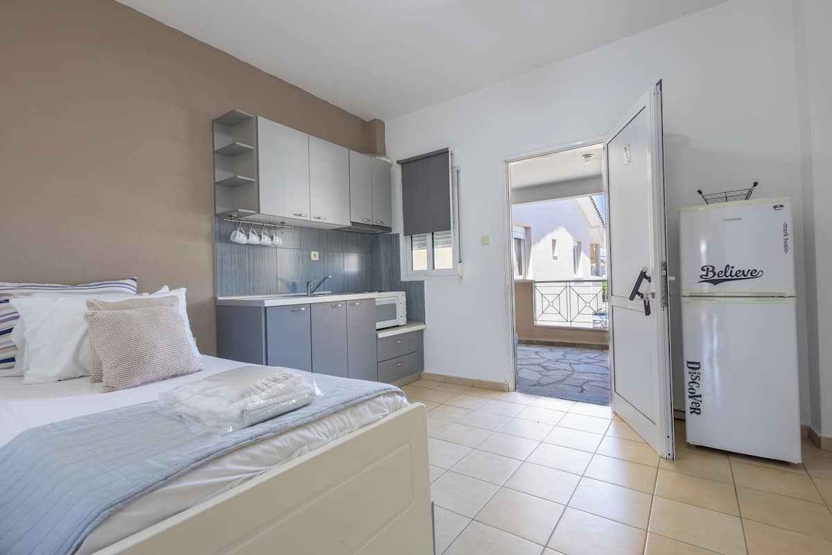 A bedroom with a bed, a kitchenette, and a refrigerator.