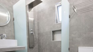 A modern bathroom with a shower, toilet, and sink. - By the Sea (Kassandra)