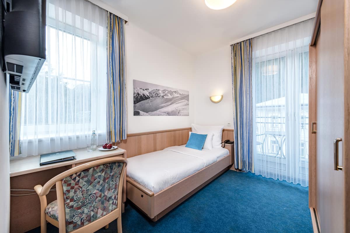 Hotellihuone, jossa on sänky, työpöytä kannettavalla tietokoneella, tuoli, yöpöytä ja ikkuna, jossa on verhot.