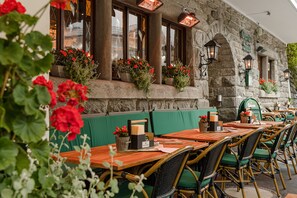 An outdoor seating area with wooden tables and wicker chairs, stone walls, and flower boxes with red flowers. - Hotel Goethehof (Bad Gastein)
