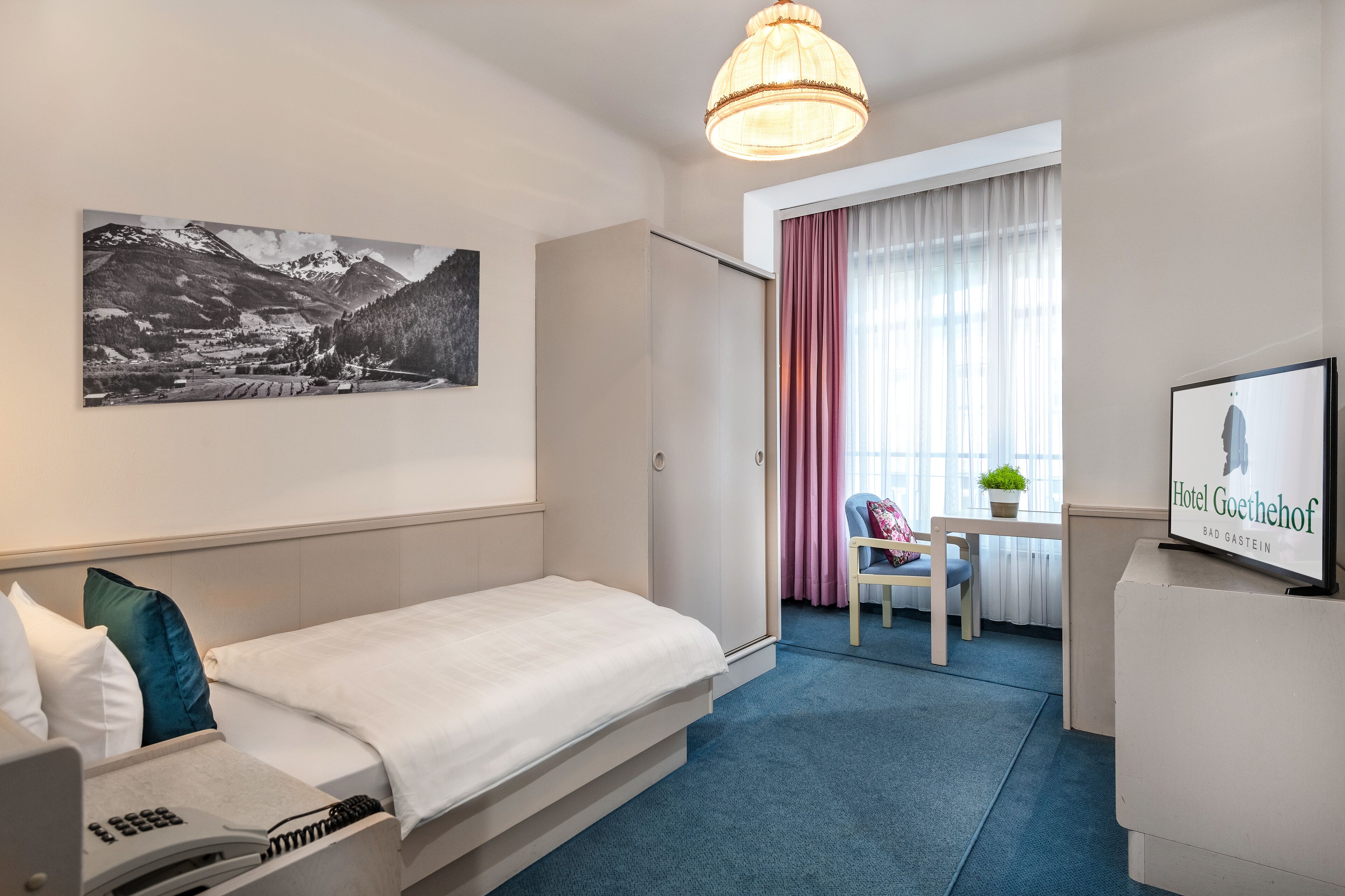 Hotelkamer met een bed, een bureau, een stoel, een lamp, een lijst en een raam met gordijnen.