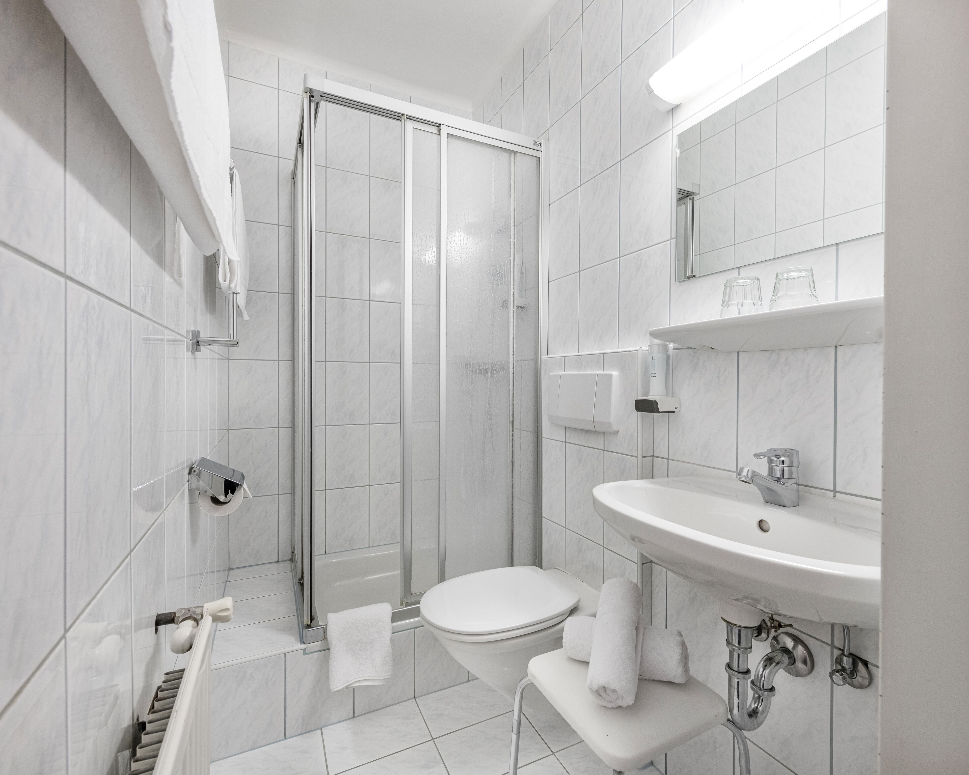 Ein modernes Badezimmer mit Duschkabine aus Glas, einer weißen Toilette und einem Waschbecken mit Spiegel darüber.