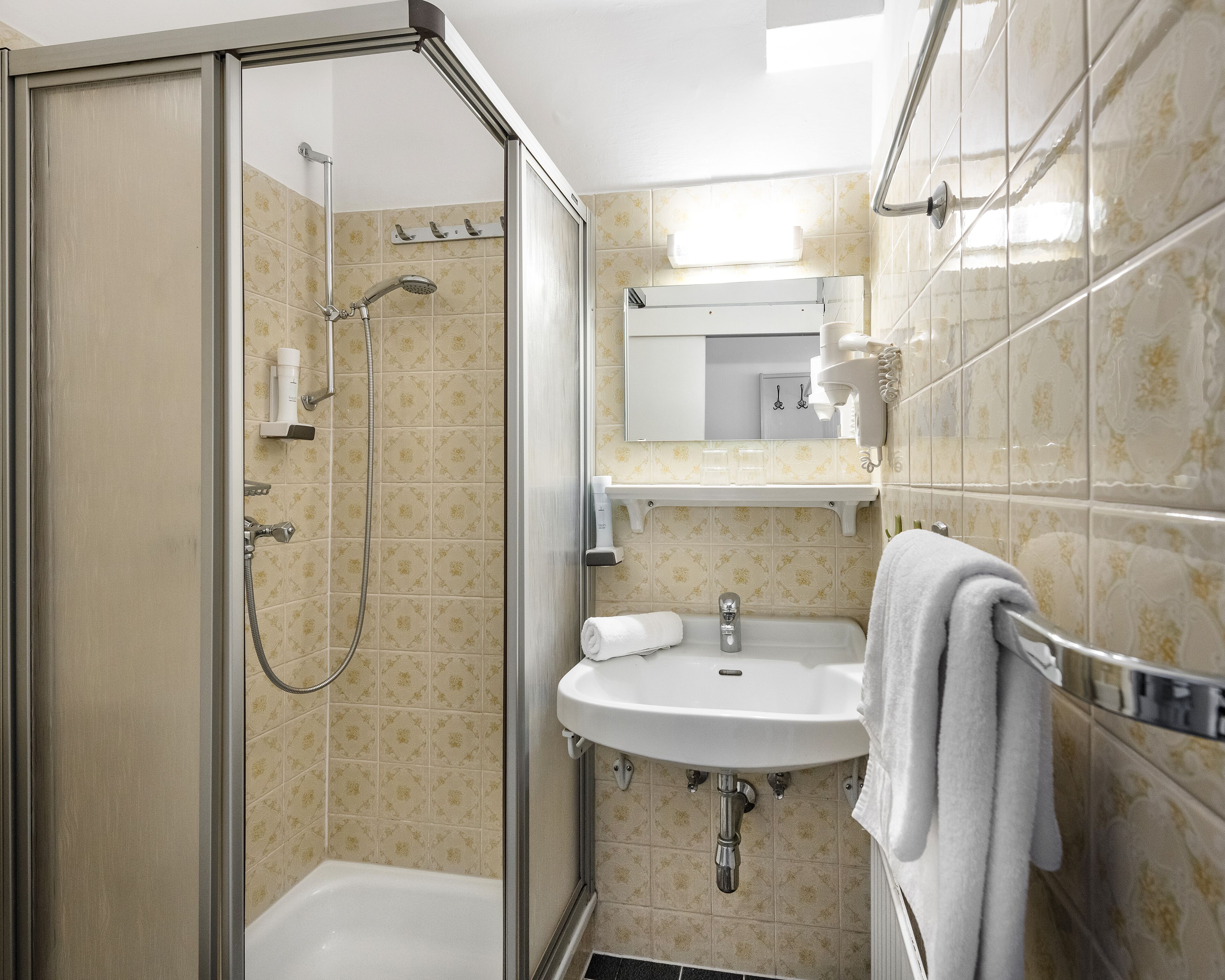 A modern bathroom with a glass-enclosed shower, a white sink, and a towel rack.