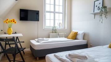 A hotel room with a bed, a desk with a chair, a TV, a window, and a plant.