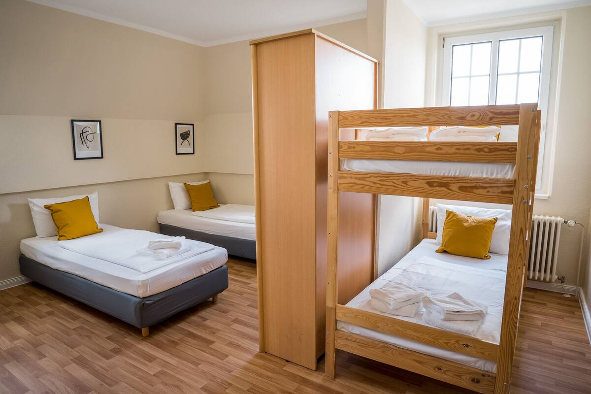 Quarto com duas camas de solteiro em beliche, um guarda-roupa e janela com persianas.
