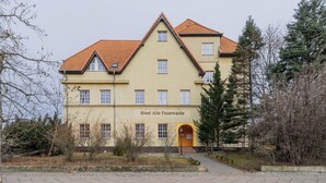 Un bâtiment à deux étages, doté d’une façade jaune et d’un toit recouvert de tuiles rouges, portant l’inscription « Hôtel Alte Feuerwache ».