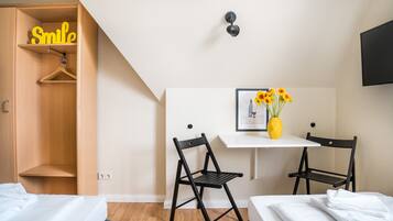 Un dormitorio con una cama, dos sillas negras, un escritorio con un jarrón de flores, una lámpara colgante y un armario con un letrero que dice 'Smile'.