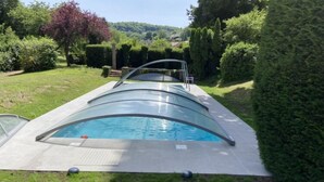 En swimmingpool med et glasafskærmning, omgivet af en velplejet græsplæne og hække.