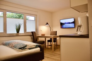 Una habitación pequeña con cama, escritorio, silla, televisor y radiador.