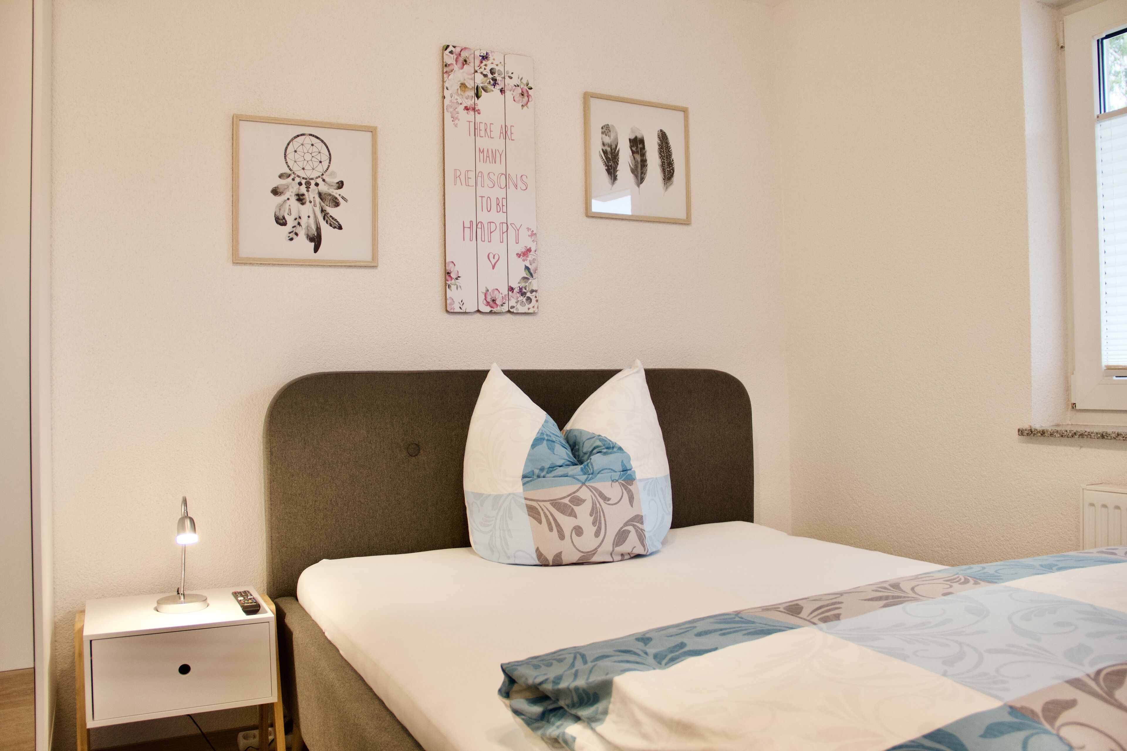 A neatly made bed with patterned bedding, a bedside lamp, a nightstand with a remote control, and decorative wall art.