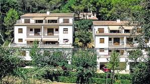 A two-story residential building with a tiled roof, balconies, and a garden area.