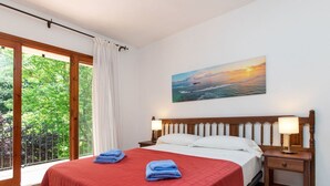 Un dormitorio con una cama grande, dos mesitas de noche con lámparas, un cuadro de un atardecer y vistas a zonas verdes a través de una puerta corredera.