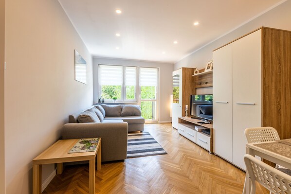 A modern living room with a sofa, a dining table, and a TV. - Victus Apartamenty - Lawendowy (Gdansk)