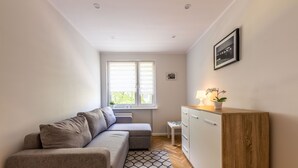 A compact living space with a sofa, a small cabinet, a window with blinds, and a patterned rug.