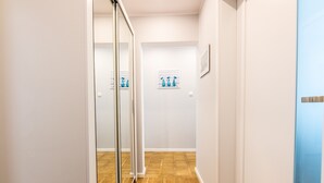 A hallway with a wooden floor, white walls, and a glass door leading to another room.