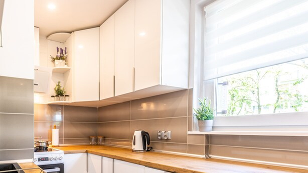 A modern kitchen with white cabinets, a wooden countertop, a stove, and a window with a view of trees.
