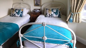 A room with two beds, each with a white headboard and a blue blanket. There is a nightstand with a lamp and a telephone between the beds. A poster is on the wall above the beds. - West Lodge Hotel (Aylesbury)