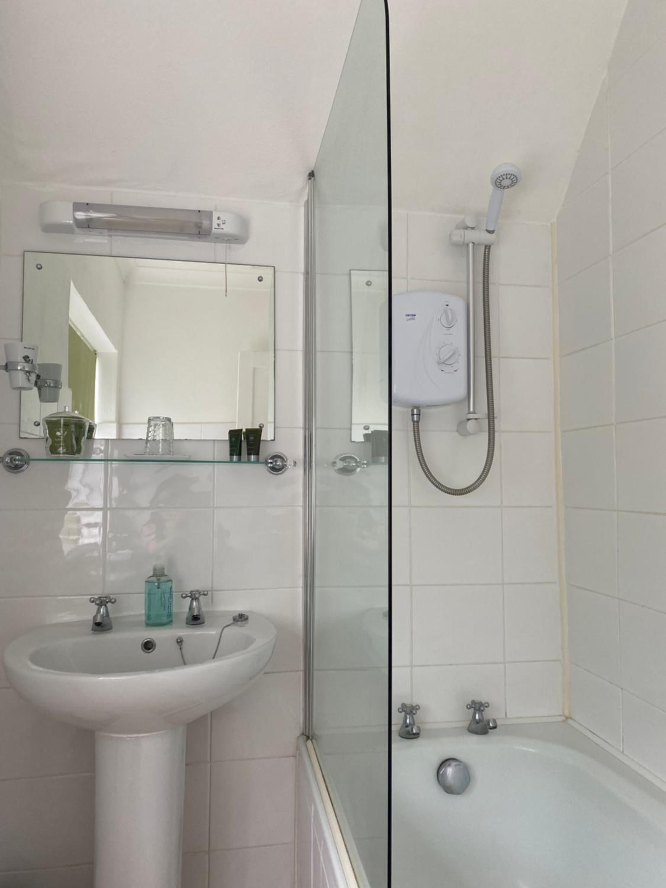 A bathroom with a glass-enclosed shower, a pedestal sink, and a mirror above the sink.