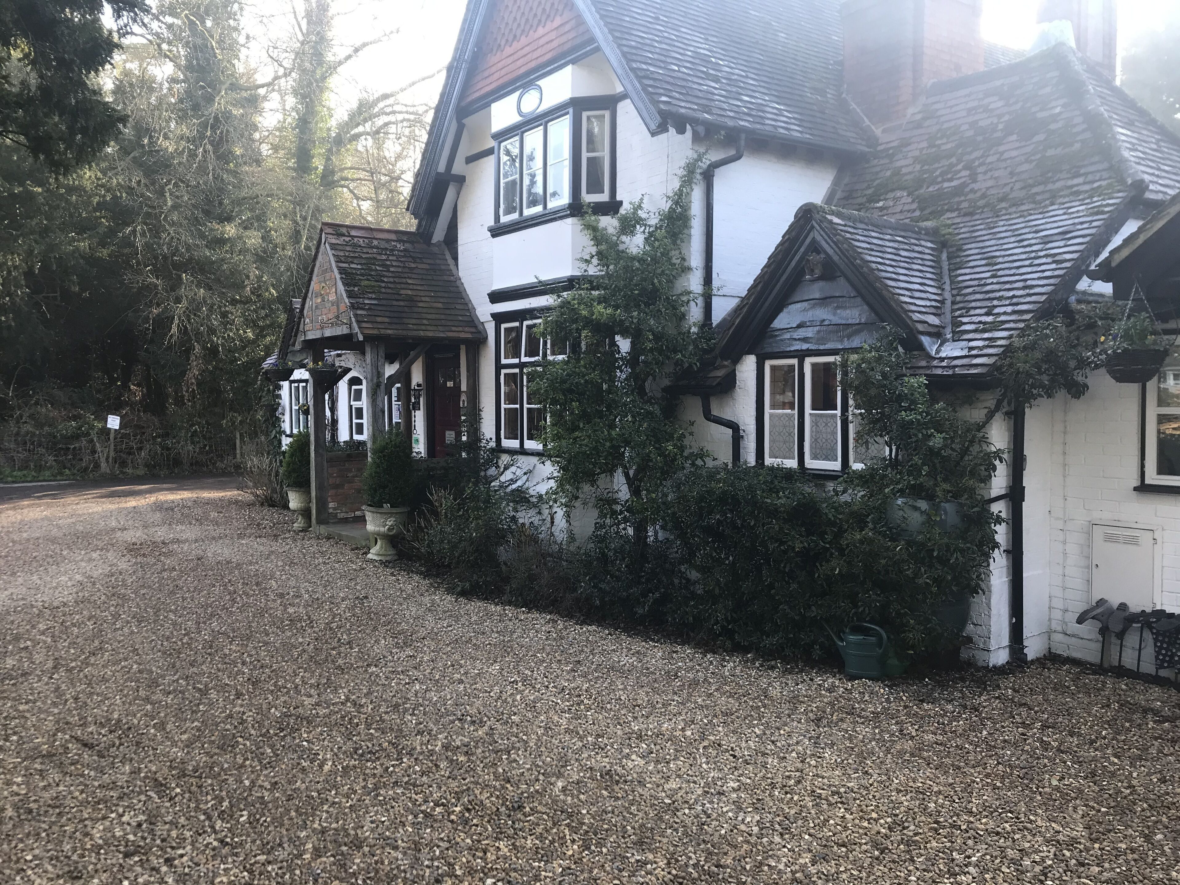Una casa tradicional de dos pisos con camino de grava y abundante vegetación alrededor.