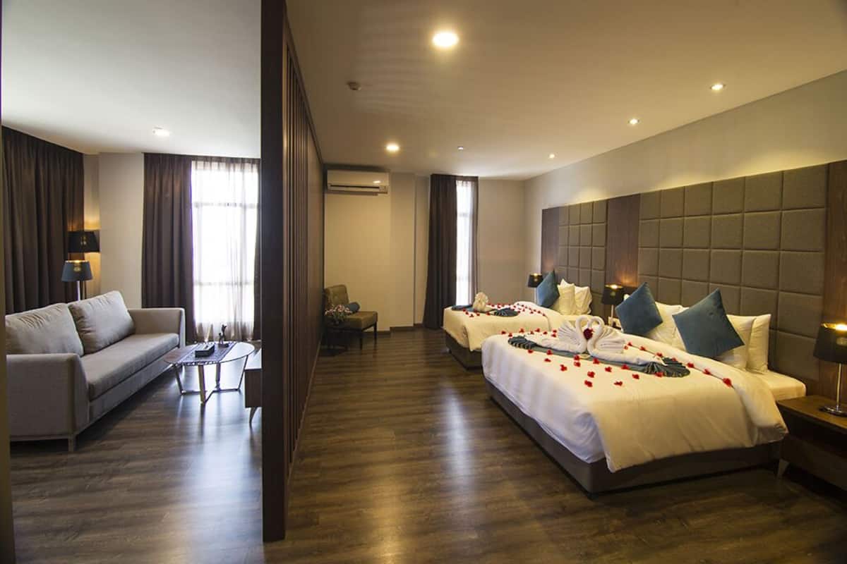 A hotel room with two beds, a sofa, a coffee table, and a lamp.