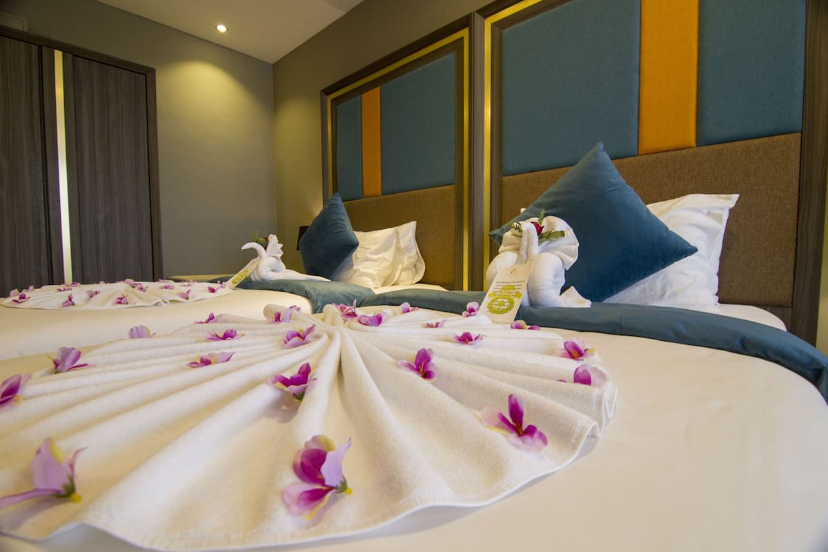 A hotel room with a neatly made bed, pillows, and a floral arrangement on the bed.