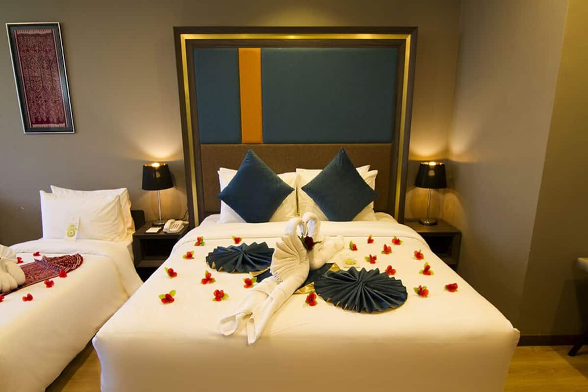 A hotel room with two beds, a large headboard, bedside lamps, and a framed artwork on the wall.