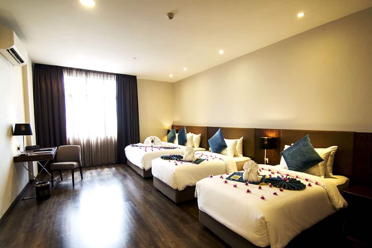 A hotel room with three beds, a desk, and a chair.