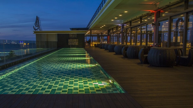Een zwembad op het dak met glazen hekwerk, uitzicht op zee en terrasmeubilair.