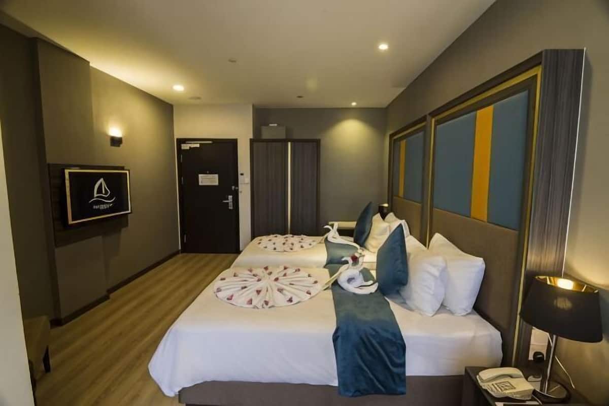 A hotel room with two beds, a desk, a chair, a phone, and a wall-mounted TV.