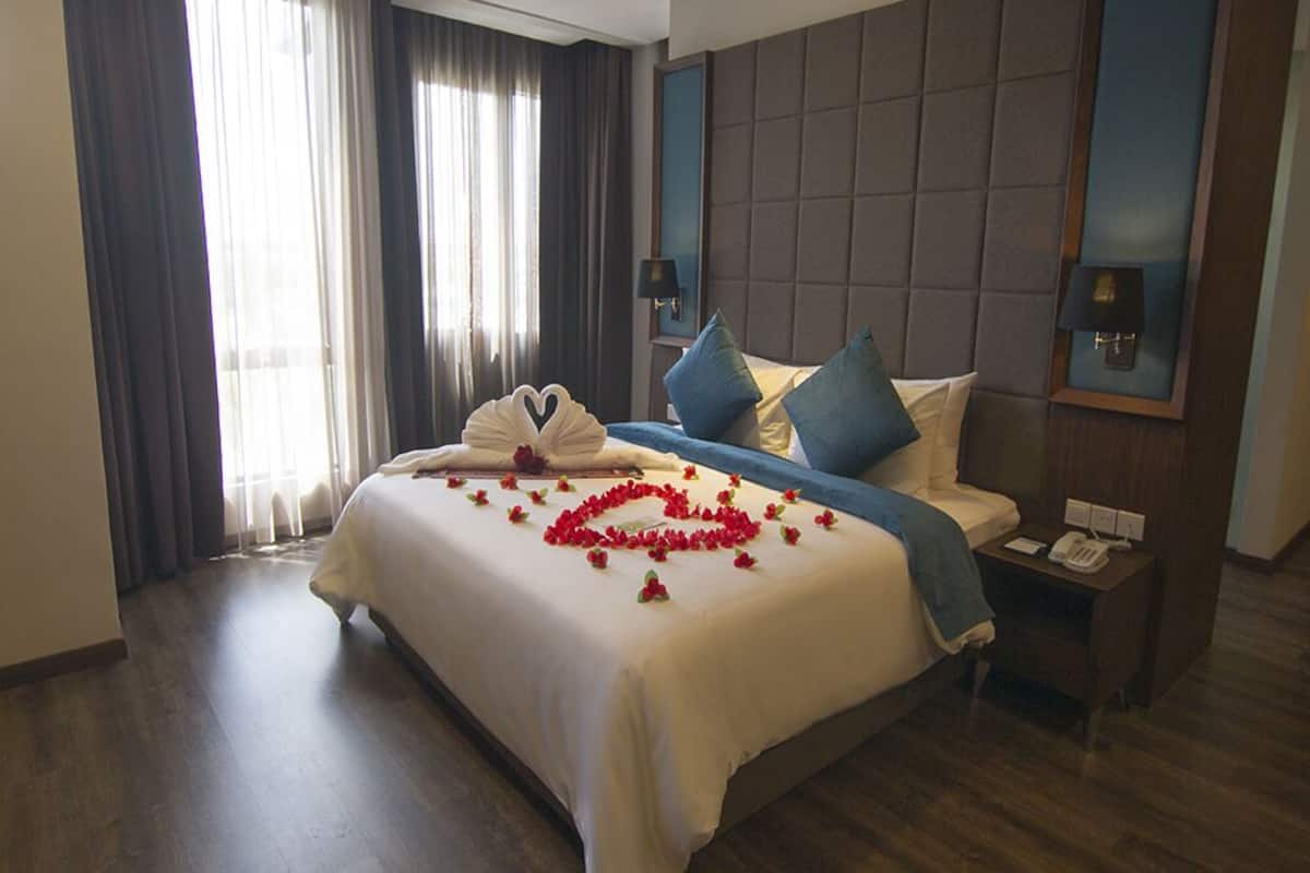 A hotel room with a large bed, a headboard, two bedside tables with lamps, and a window with curtains.