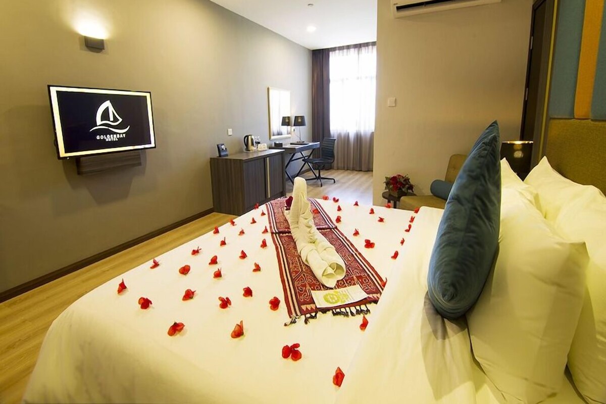 A hotel room with a bed, a desk, a chair, a television, and an air conditioning unit.
