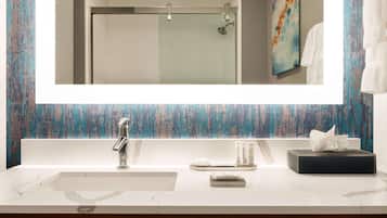 A bathroom with a large mirror, a sink, a shower, and a towel rack.