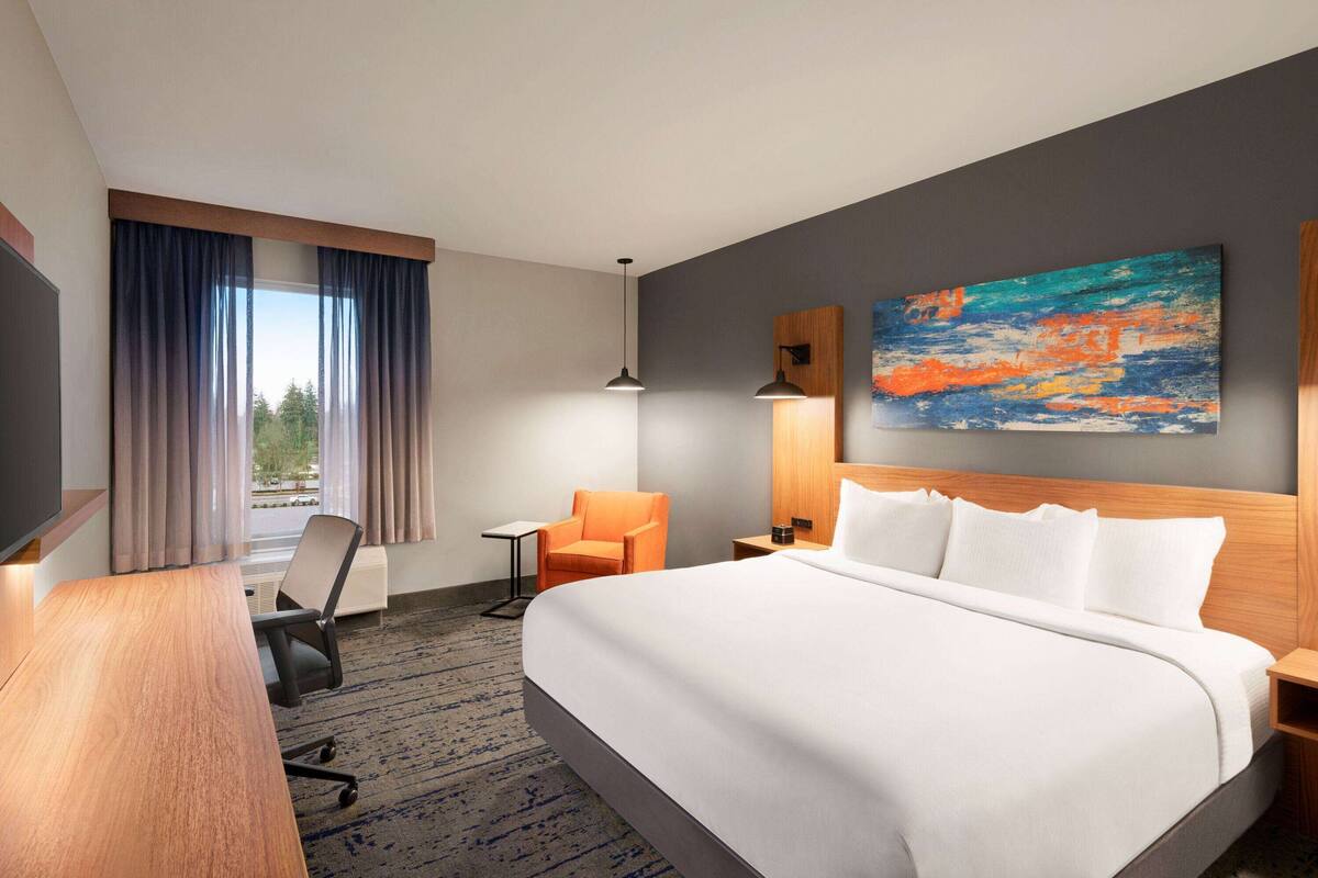 Ein Hotelzimmer mit einem großen Bett, einem Schreibtisch, einem Stuhl, einem Bild an der Wand und einem Fenster mit Vorhängen.