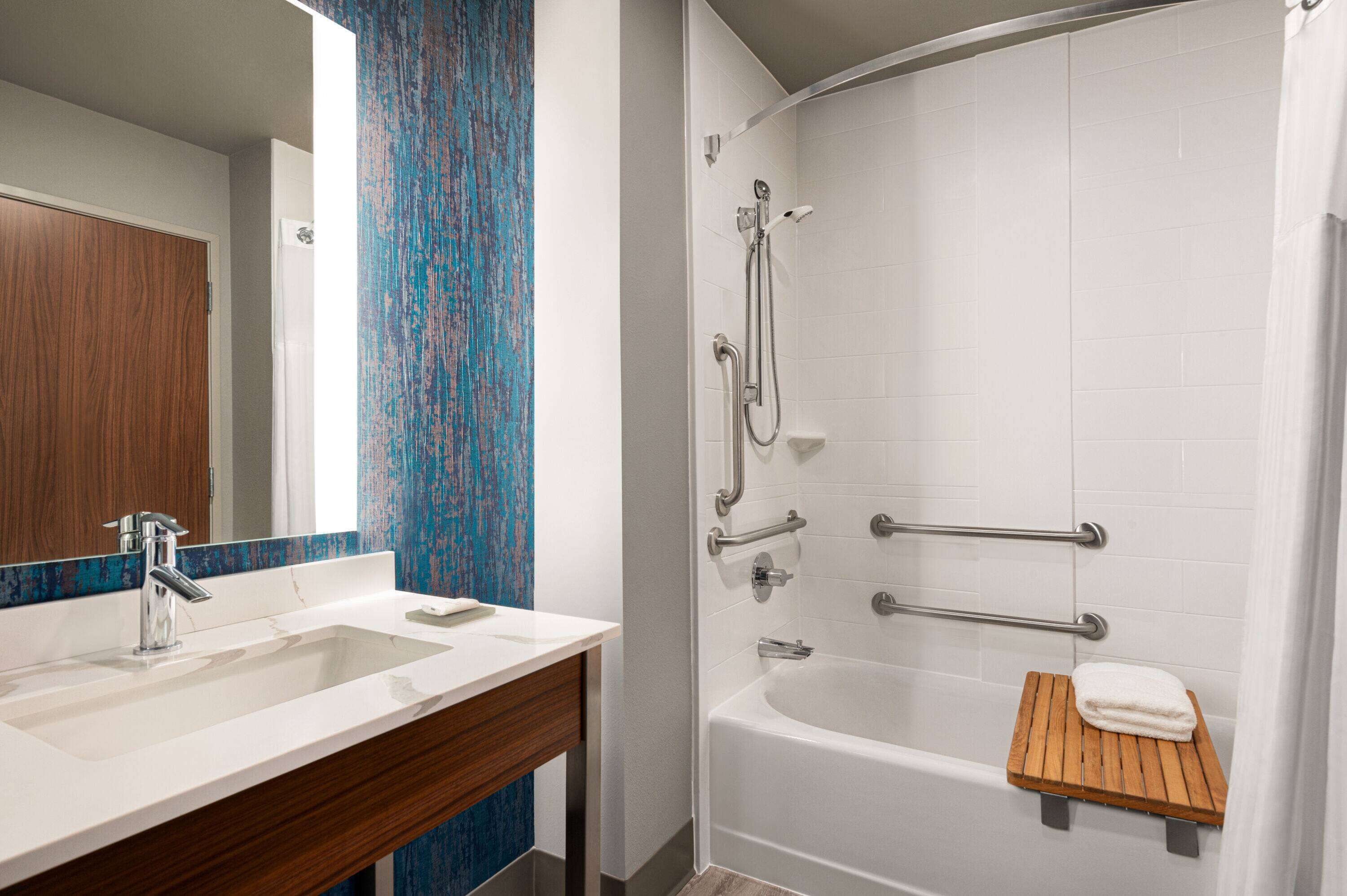 A bathroom with a white sink, wooden vanity, and a shower with grab bars.