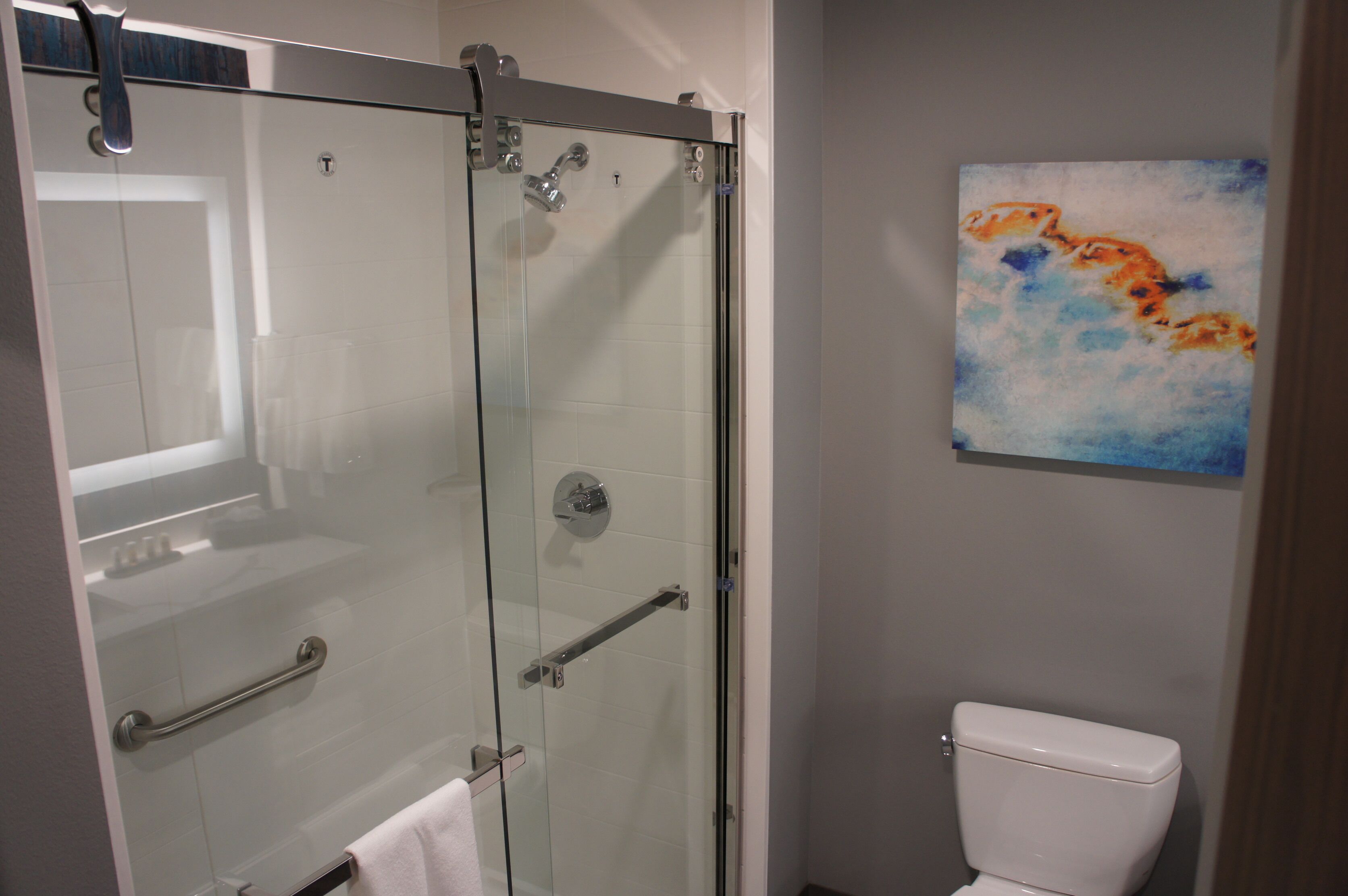 A bathroom with a glass-enclosed shower, a white toilet, and a painting on the wall.