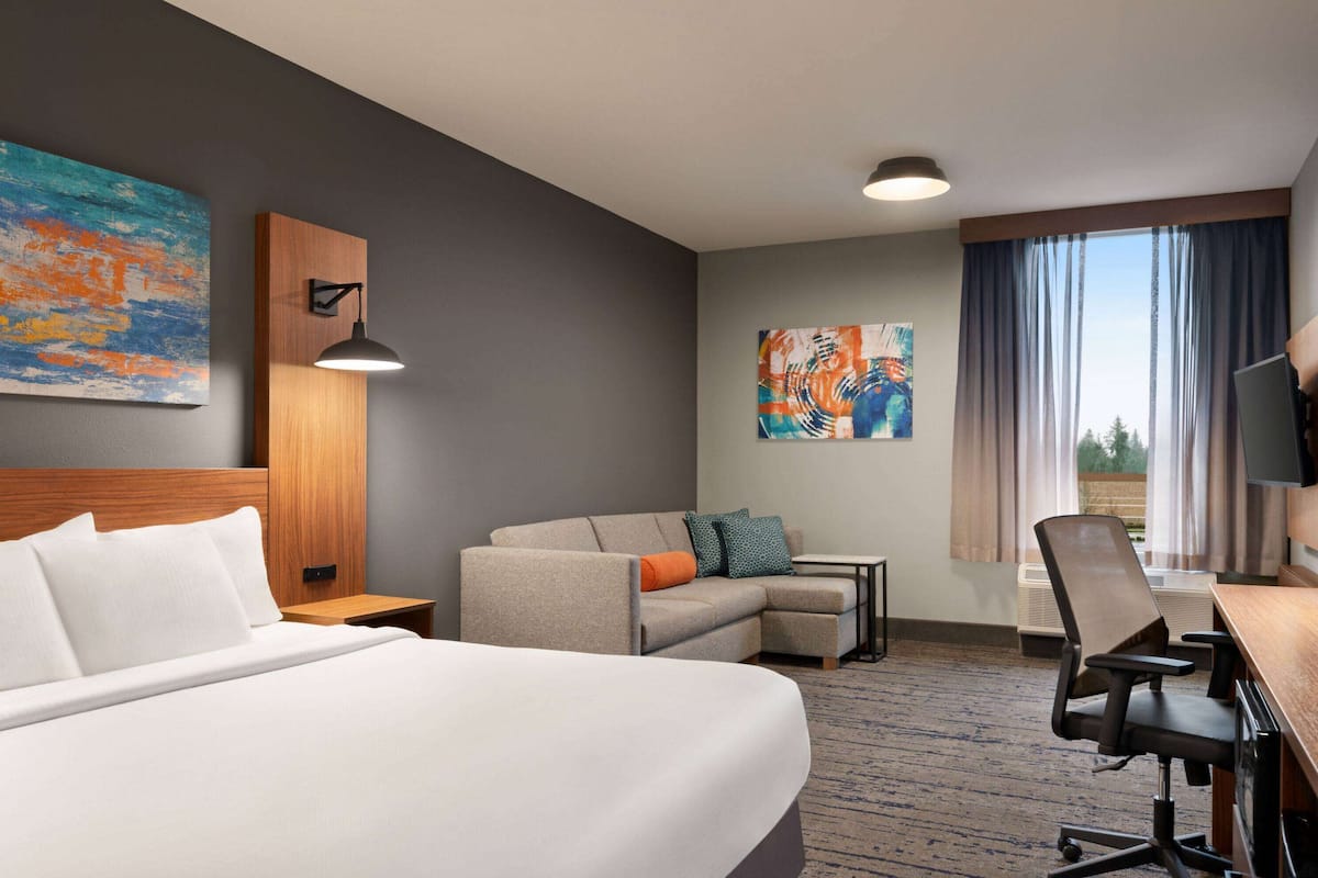 Ein Hotelzimmer mit einem Bett, einem Schreibtisch, einem Sessel und einem Sofa, sowie Kunstwerken an den Wänden.
