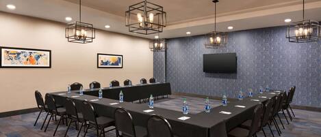A conference room with a long table, chairs, water bottles, and a flat-screen TV on the wall.