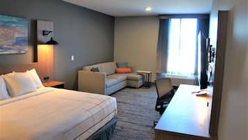 A hotel room with a bed, a desk, a chair, a sofa, and a TV.
