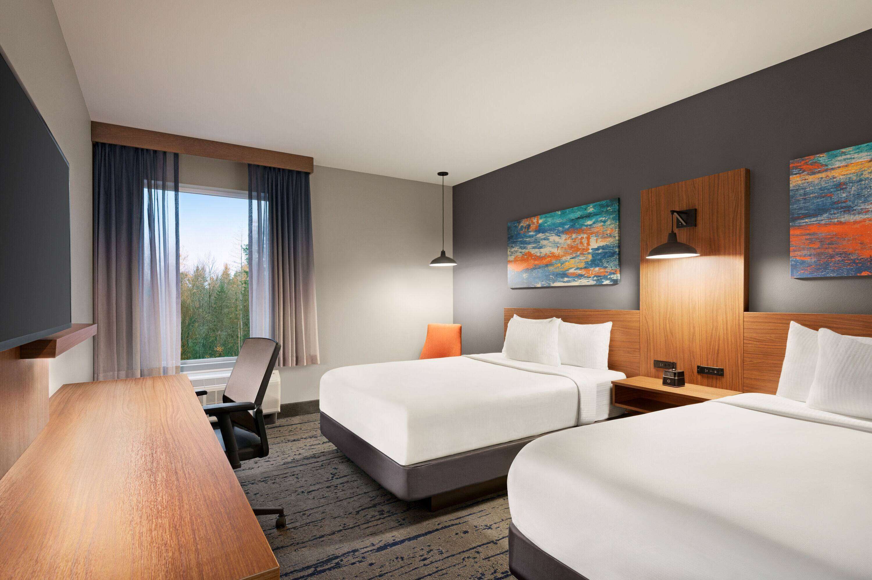 A hotel room with two beds, a desk, and a large window with curtains.